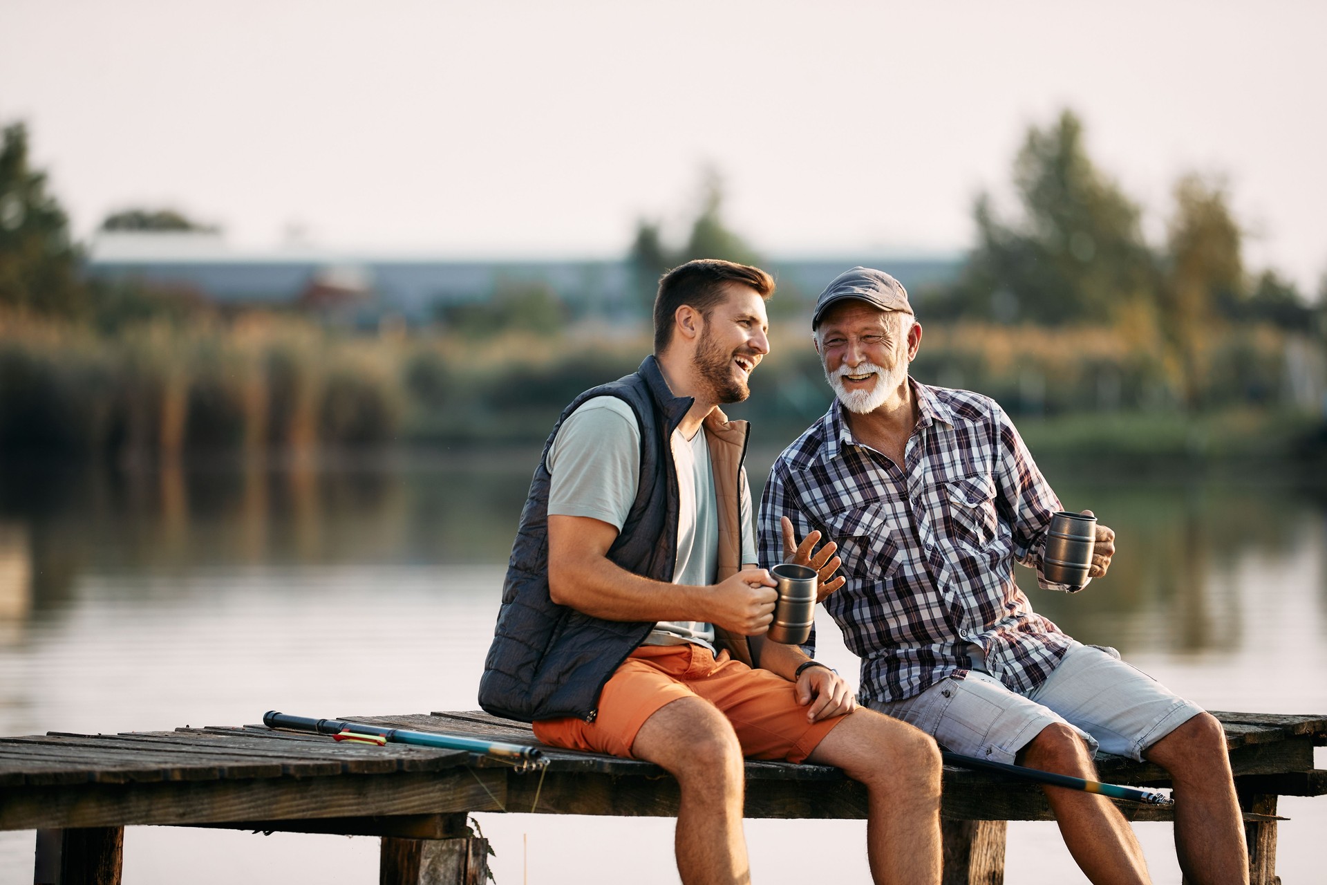 Cheerful man and his mature father having fun while fishing from a pier.